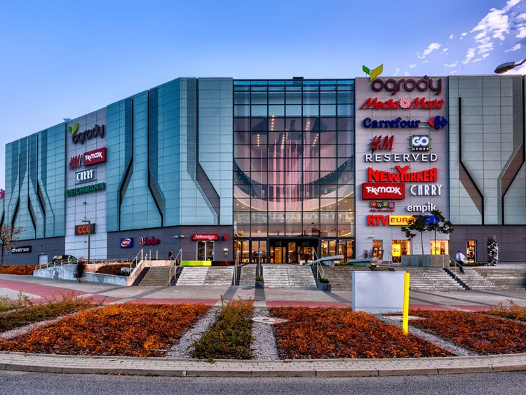 Photo: Ogrody Elbląg: Modern glass façade with lots of different company logos; green areas in the foreground